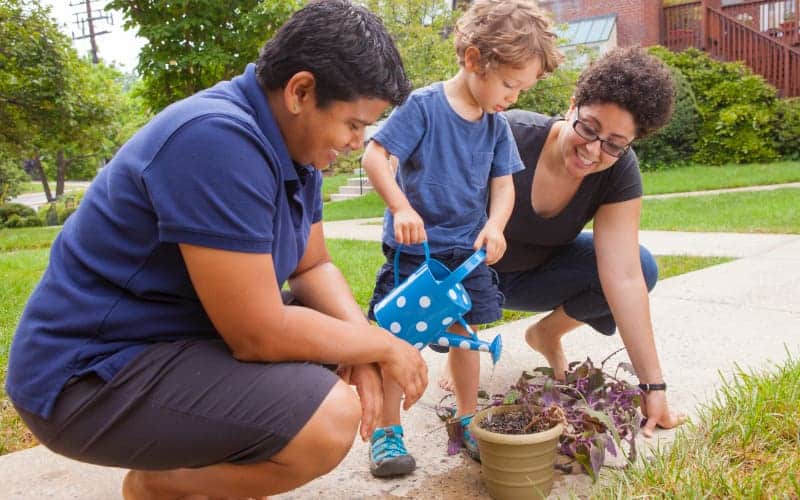 A young boy watering plants with his moms