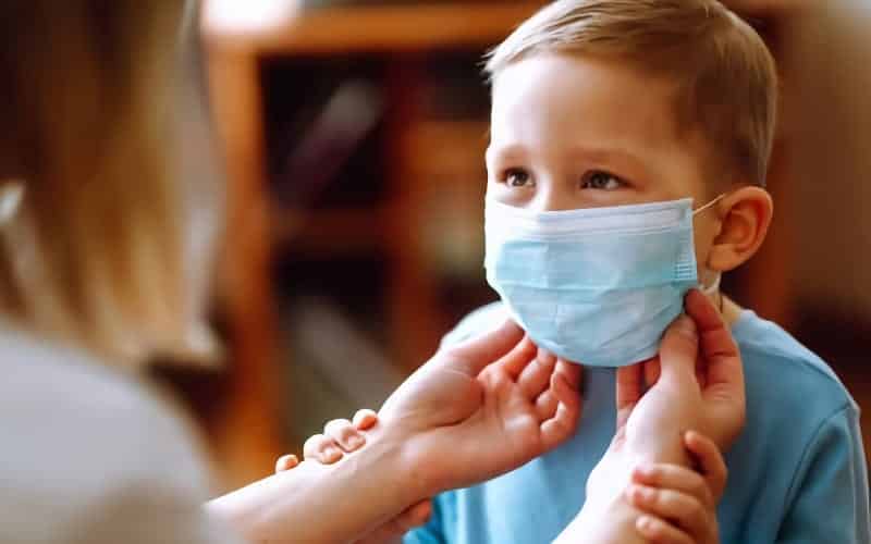 A woman adjust a face mask on a young boy