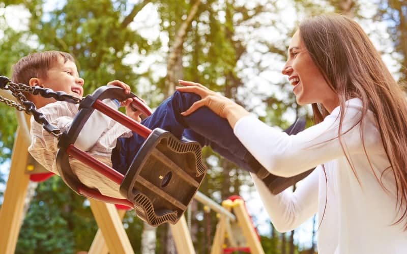 Mother pushes her small son in a swing at the park