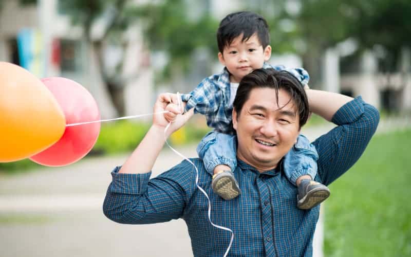 Asian father holds his young son on his shoulders at the park